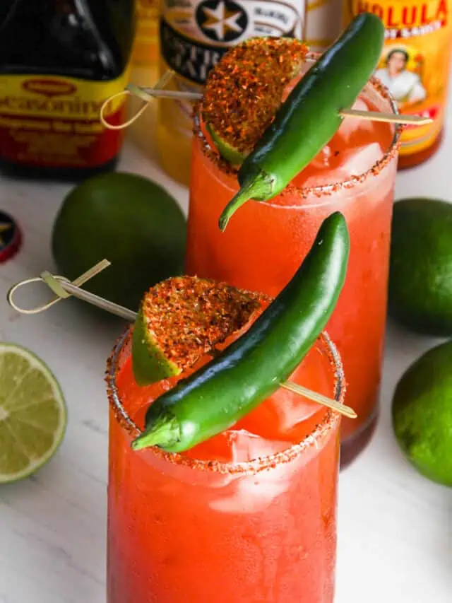 A tall glass filled with michelada garnished with green chili and spice coated lime slice.
