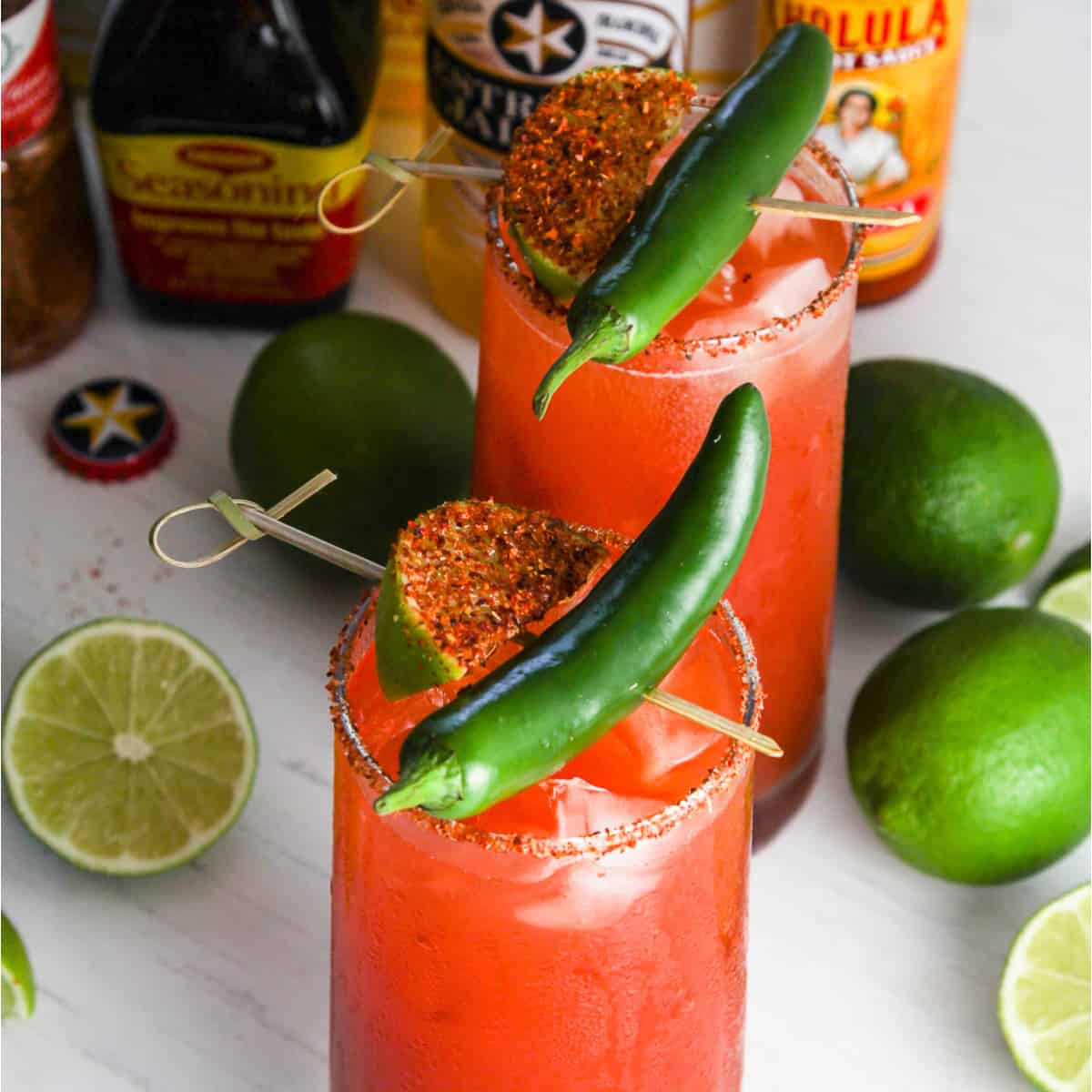 A tall glass filled with michelada garnished with green chili and spice coated lime slice.