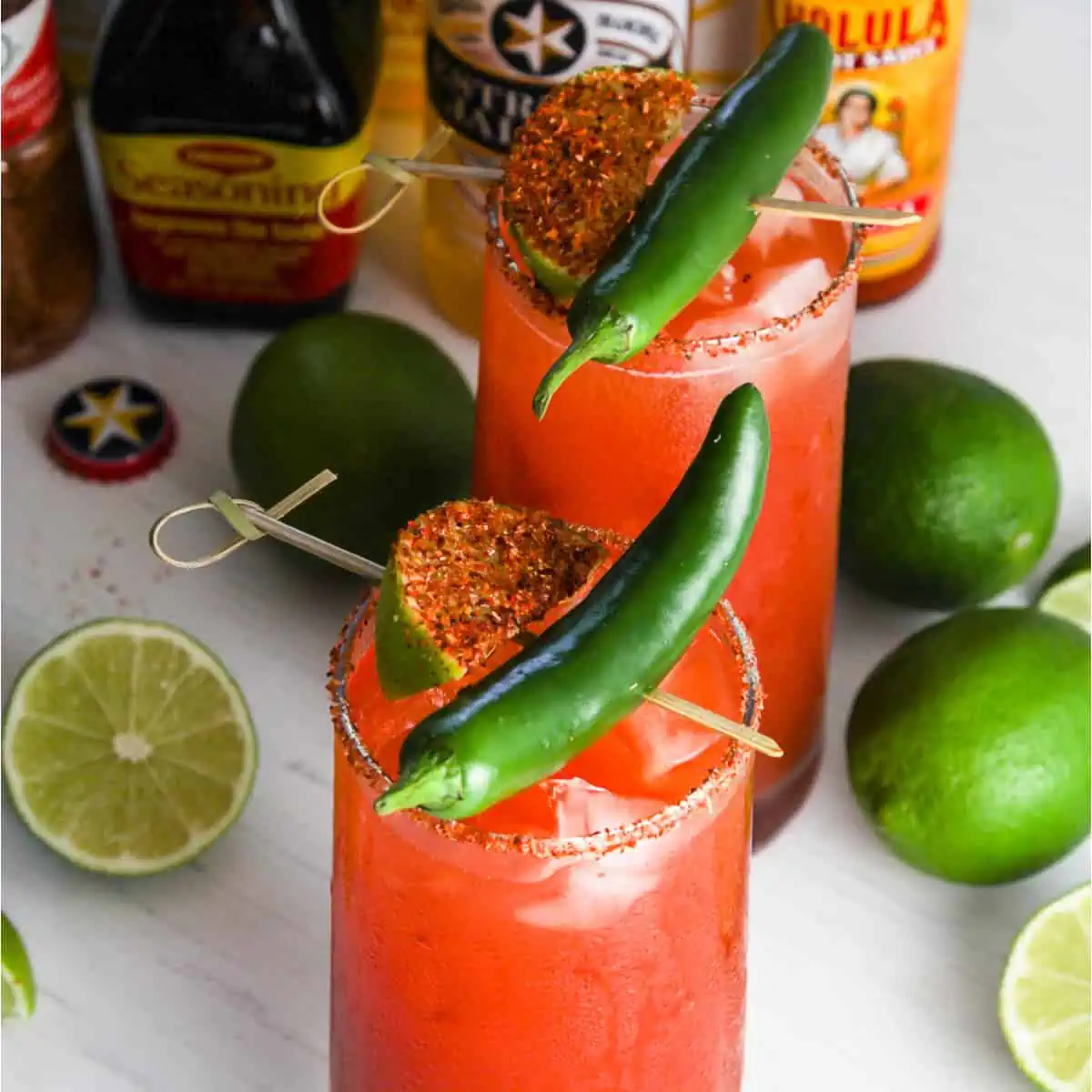 A tall glass filled with michelada garnished with green chili and spice coated lime slice.