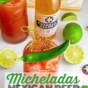 Homemade Micheladas in tall clear glasses and garnished with a chile pepper and a slice of lime with Mexican beer bottles in the background.