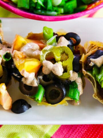 Small mini tacos topped with black olives, tomato, green onions, cheese and crema sauce.