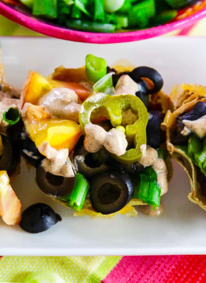 Small mini tacos topped with black olives, tomato, green onions, cheese and crema sauce.