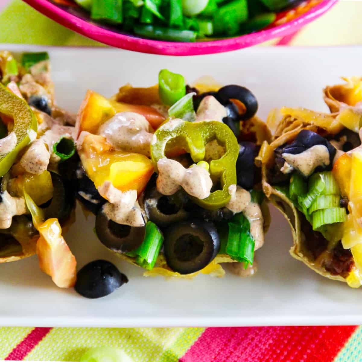 Small mini tacos topped with black olives, tomato, green onions, cheese and crema sauce.