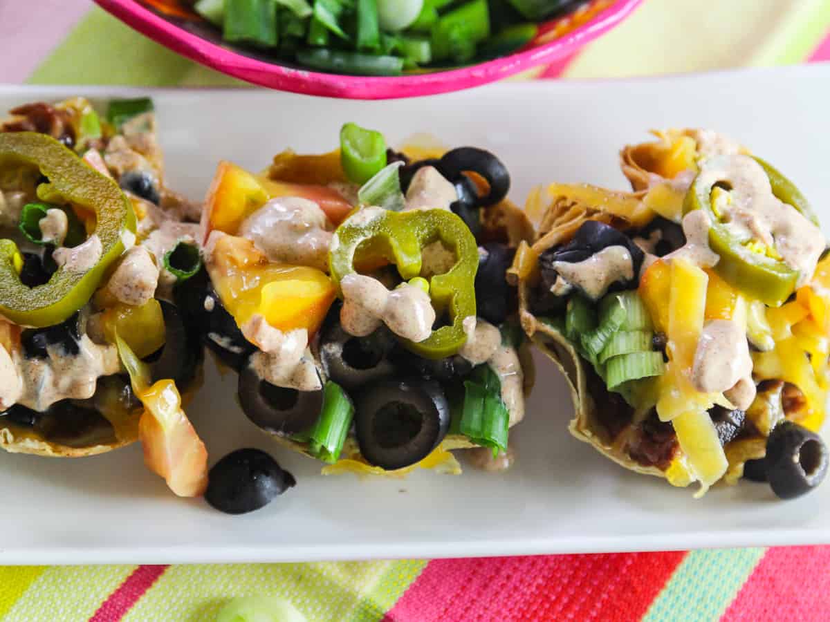Mini Tacos baked in flour tortillas topped with tomatoes, black olives, and pickled jalapenos.