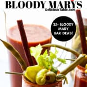 A glass pitcher full of spicy bloody mary mix and two glasses filled with it and garnished with celery, stuffed olives, and pickled green beans.