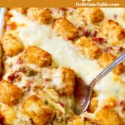 A white rectangle casserole dish filled with a brown and bubbly tater tot breakfast casserole with a silver serving spoon scooping out a piece.