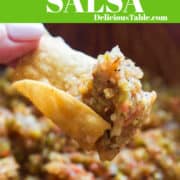 A lady holding a curved tortilla chip that scooped up tomatillo salsa and is ready to take a bite.