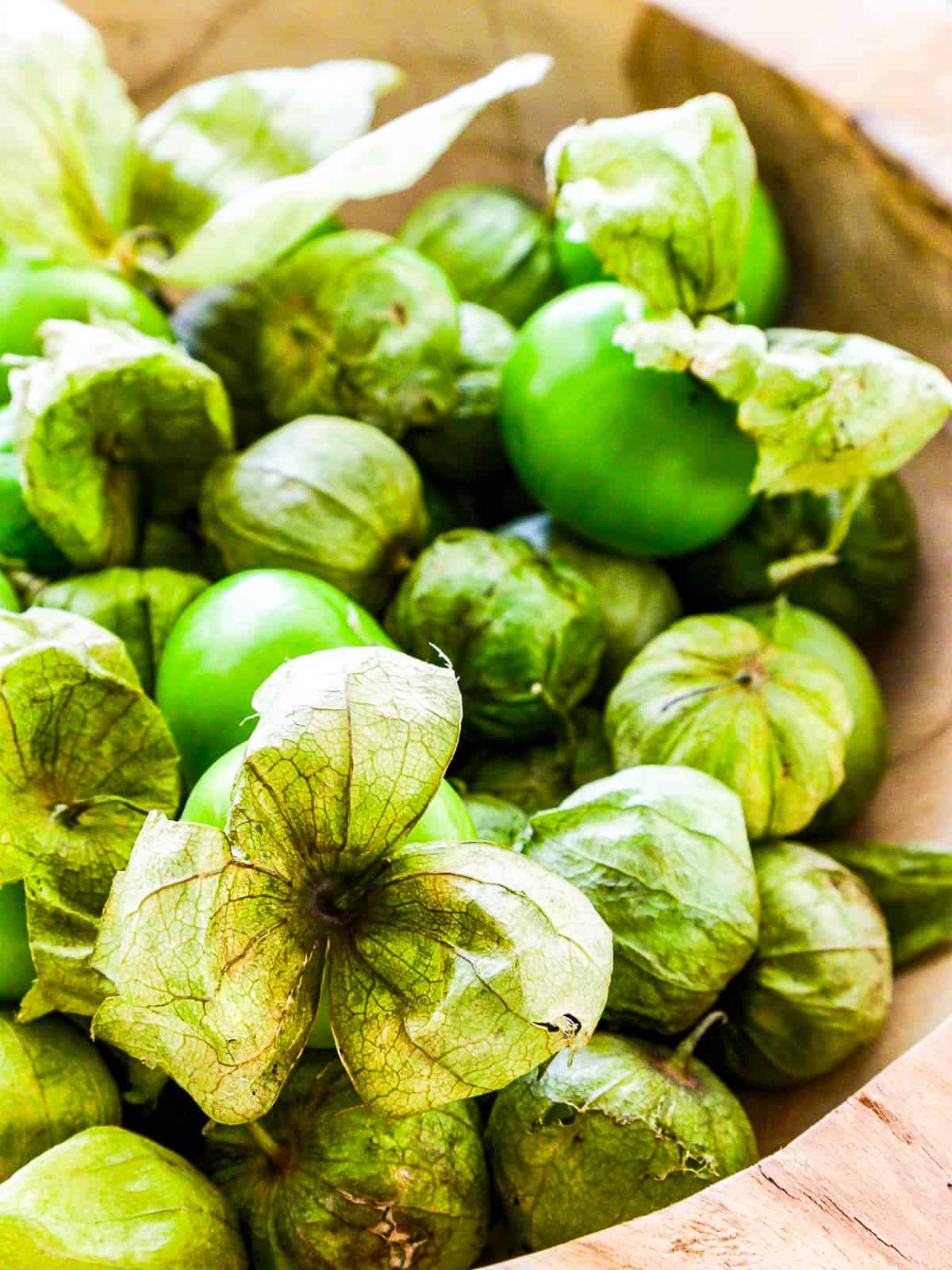A wooden bowl with fresh green tomatillos ready to remove the paper husks and use in a Mexican food recipe.