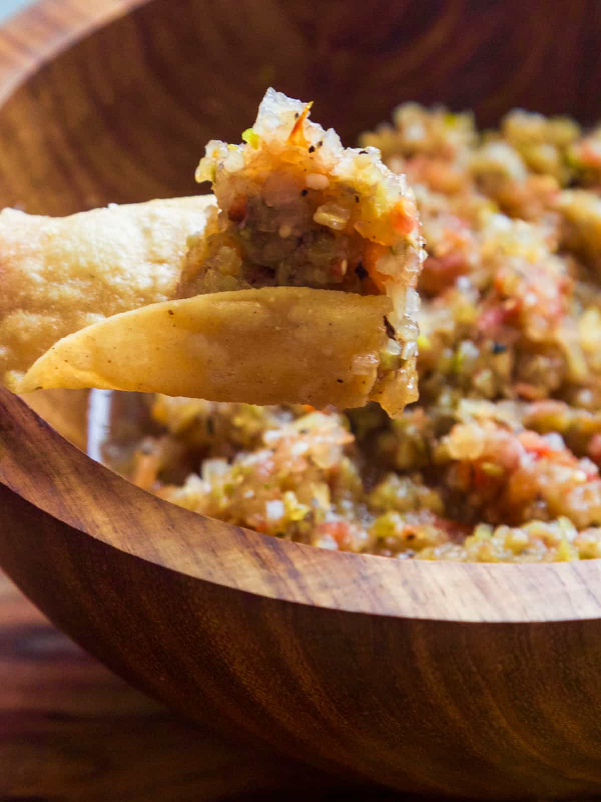A wooden bowl with a curved tortilla scoop of homemade tomatillo salsa on it ready to take a bite.