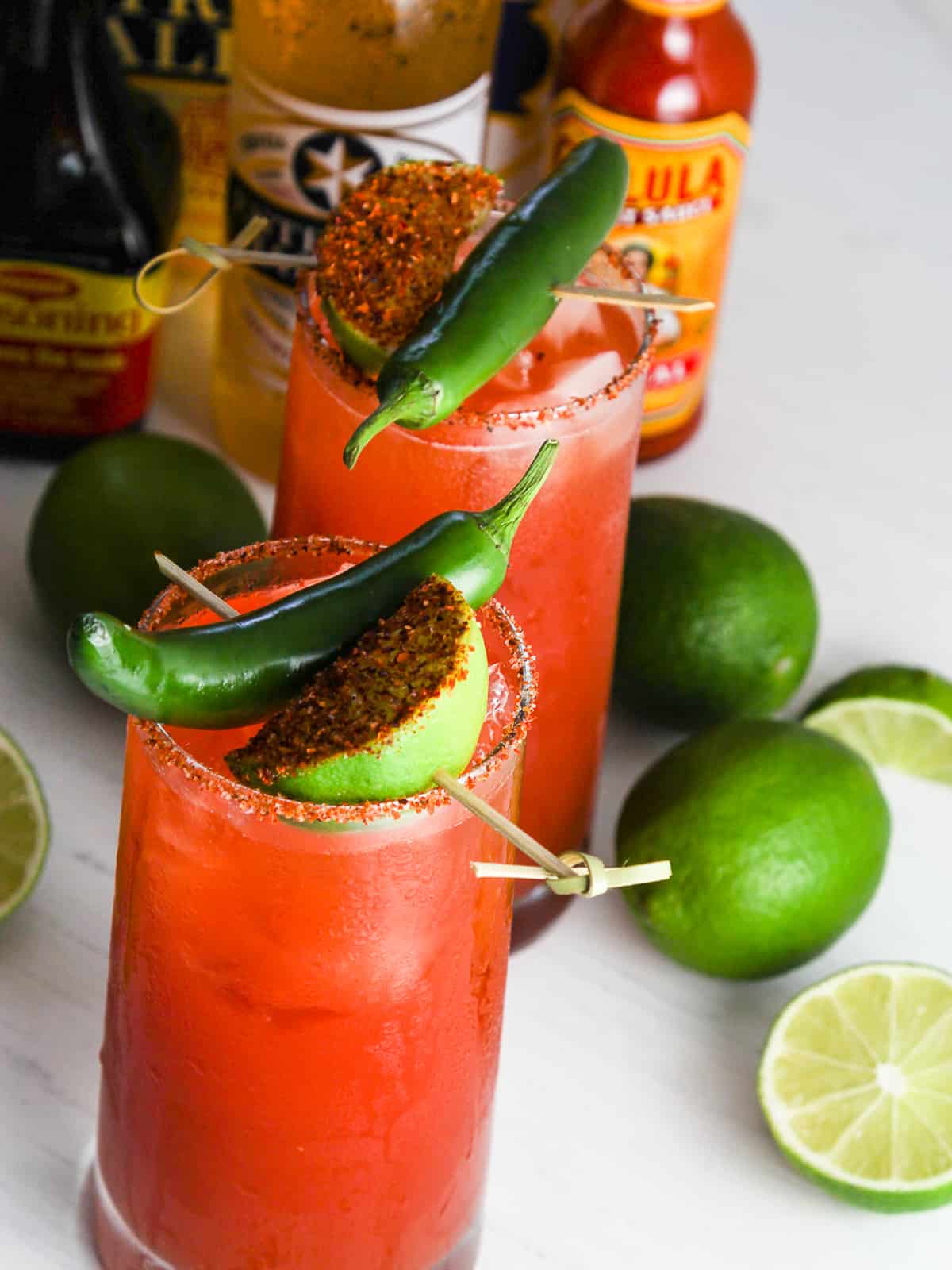 Two glasses of spicy michelada cocktails garnished with lime and chiles.
