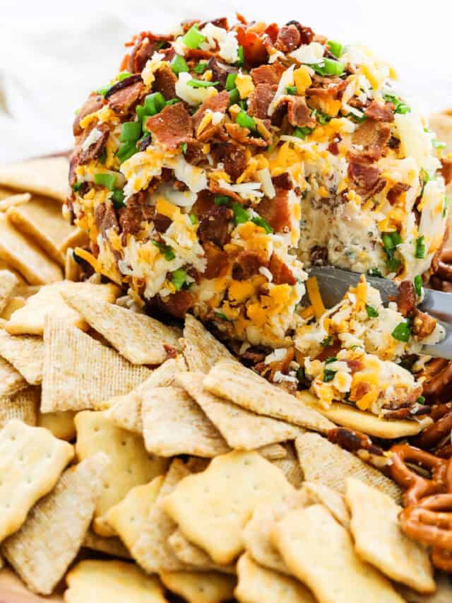 A round bacon cheese ball topped with bacon, cheddar cheese, and surrounded by crackers and pita chips for an easy appetizer.