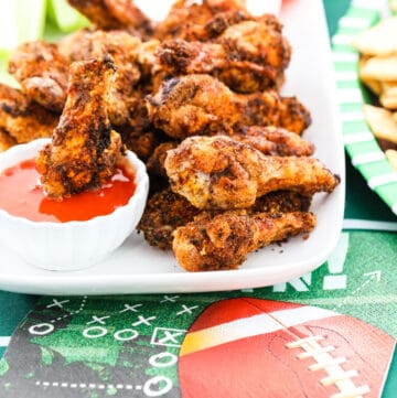 A white platter filled with crispy chicken wings and one dipping into buffalo sauce.
