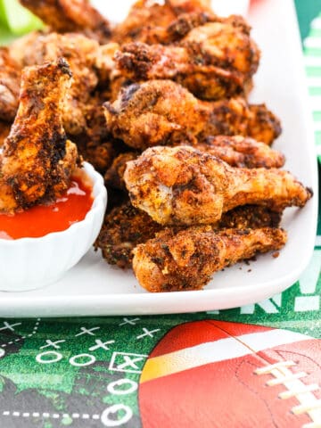 A white platter filled with crispy chicken wings and one dipping into buffalo sauce.