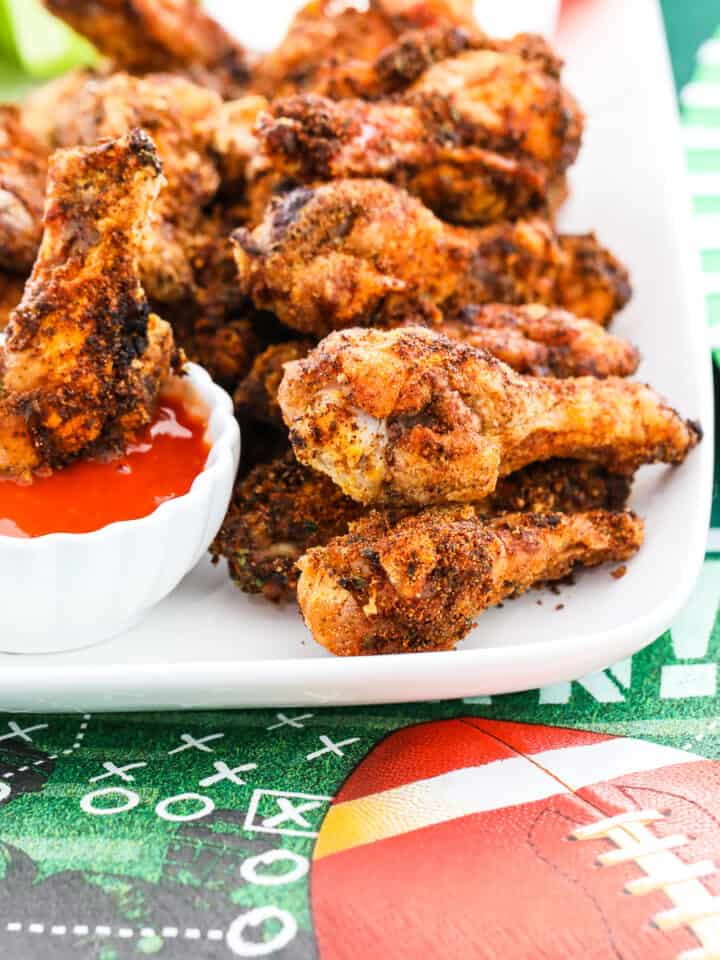 A white platter filled with crispy chicken wings and one dipping into buffalo sauce.