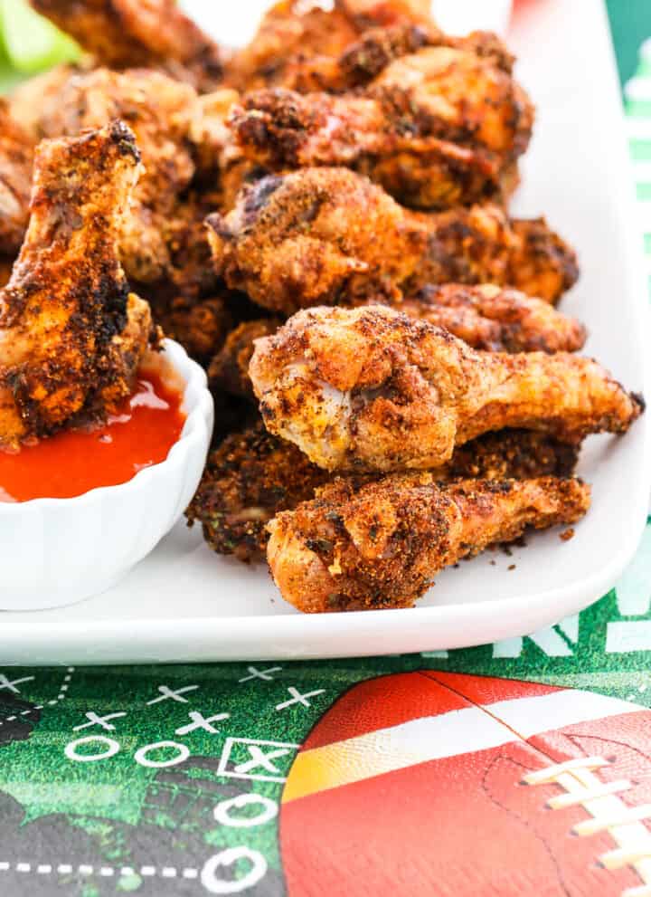 A white platter filled with crispy chicken wings and one dipping into buffalo sauce.