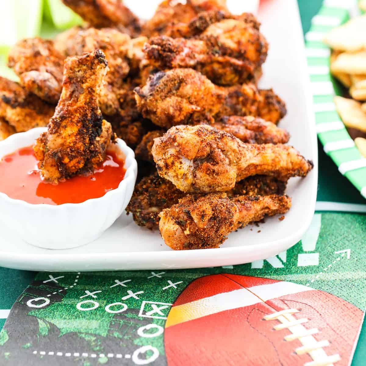 A white platter filled with crispy chicken wings and one dipping into buffalo sauce.