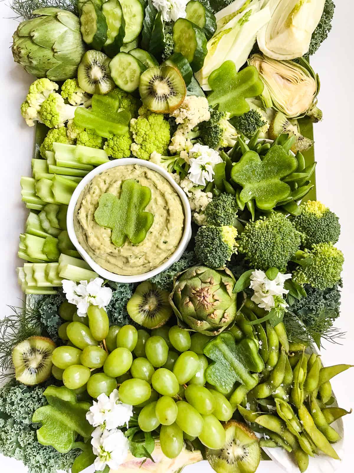 A large green food vegetable and fruit tray with a green dip in a white bowl for St Patrick's Day.