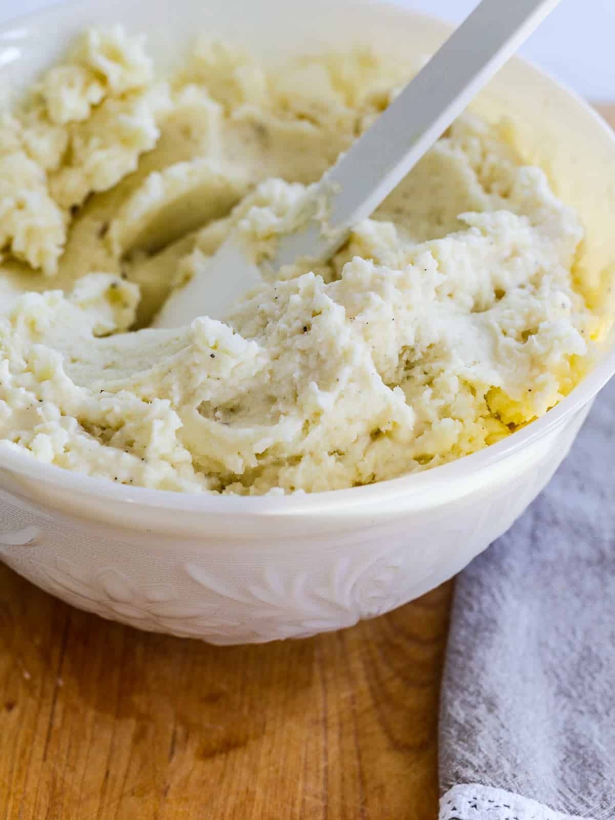 A large white spatula inside a white bowl filled with fluffy mashed potatoes.