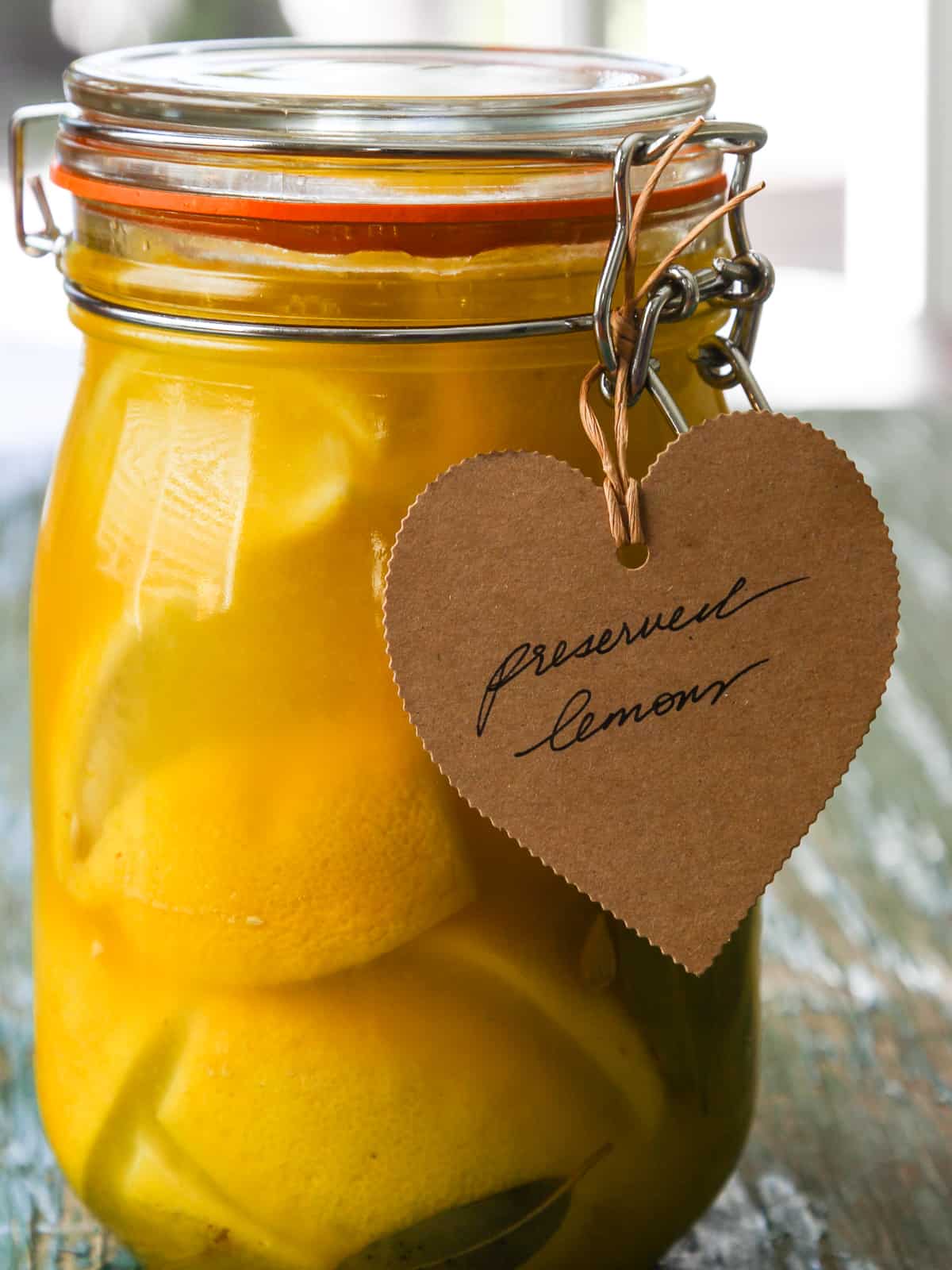 Close up of a jar of preserved lemons with a brown paper tag on it that says preserved lemons. 