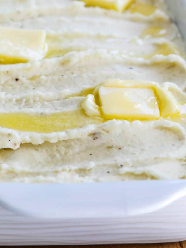 A white casserole dish filled with mashed potatoes and squares of melted butter on top.
