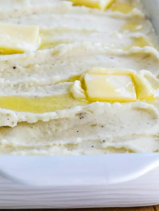 A white casserole dish filled with mashed potatoes and squares of melted butter on top.
