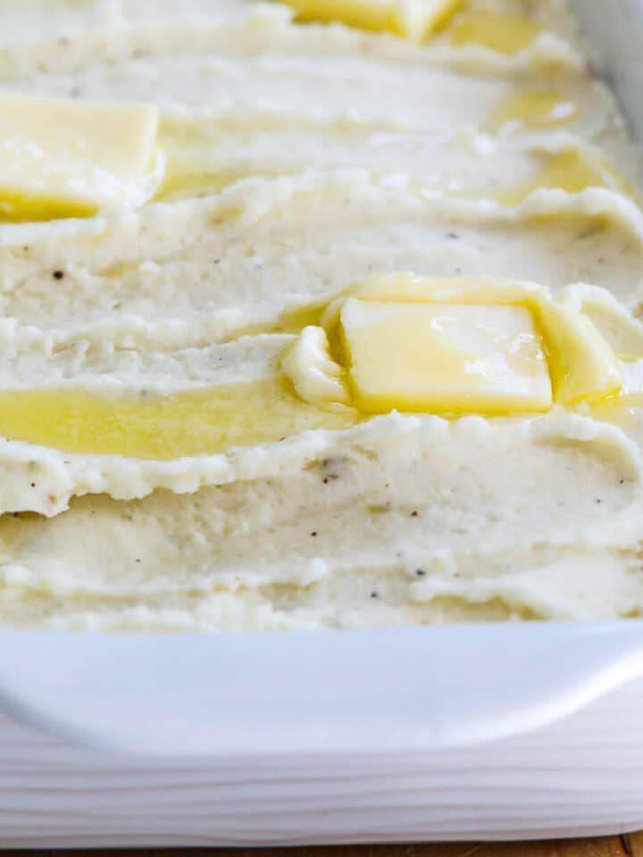 A white casserole dish filled with mashed potatoes and squares of melted butter on top.