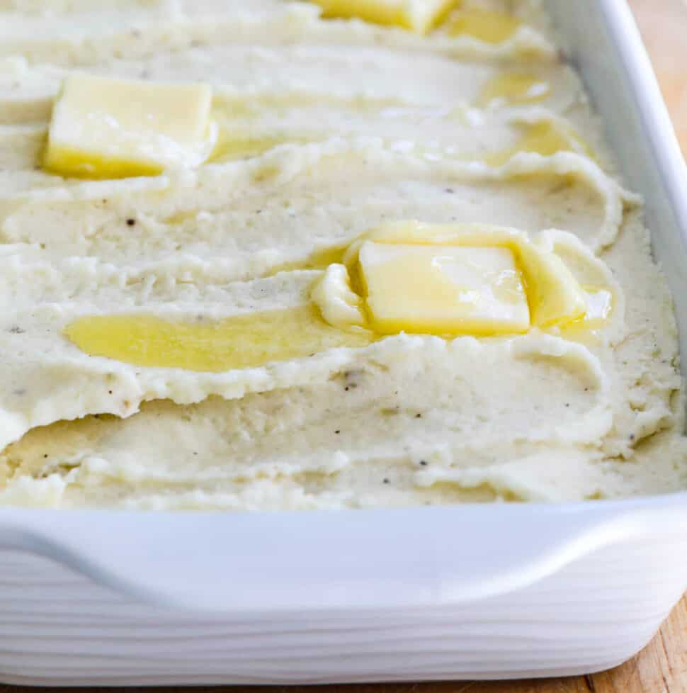 A white casserole dish filled with mashed potatoes and squares of melted butter on top.