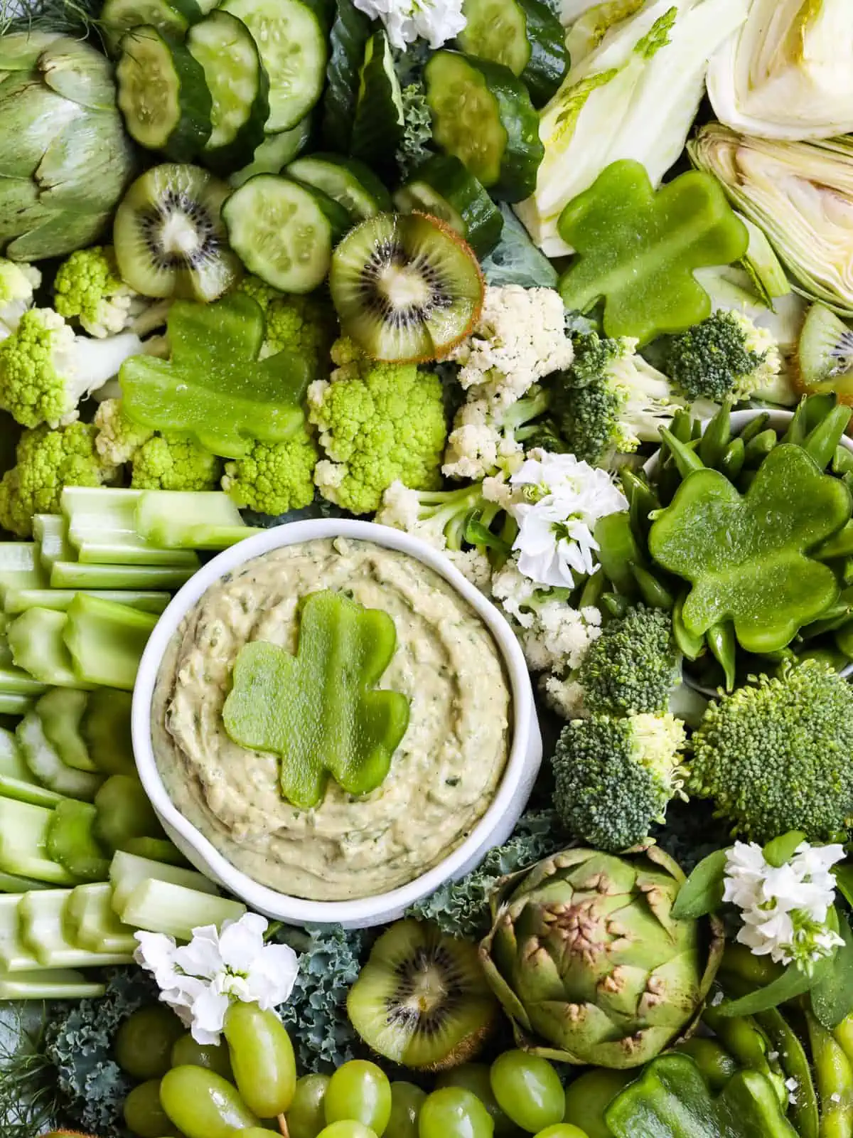 An all green vegetable tray for St. Patrick's Day with cut veggies and fruit with a dip.