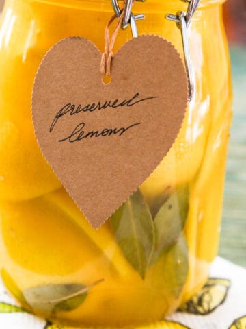 A large clamp jar of Preserved Lemons with a brown craft paper tag that says Preserved Lemons.