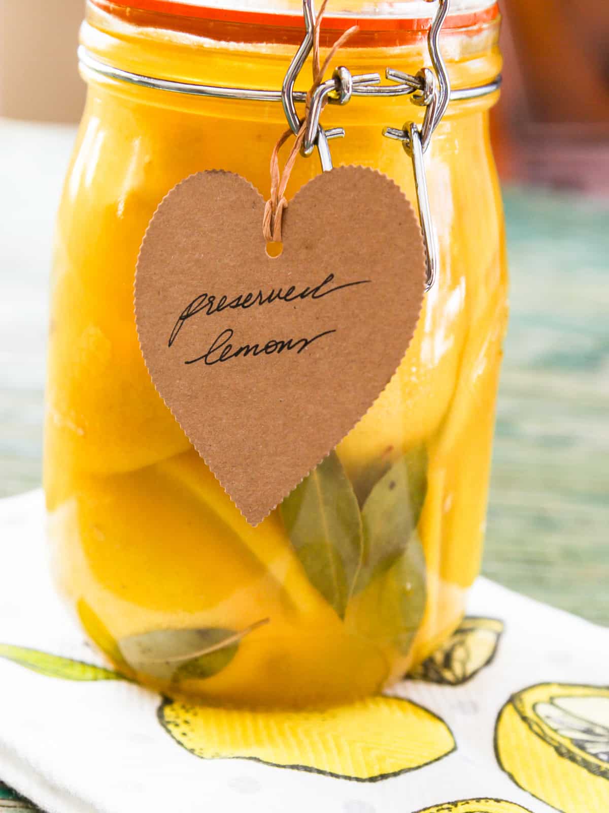 A tall clamp jar filled with preserved lemons, bay leaves, and a brown paper tag.