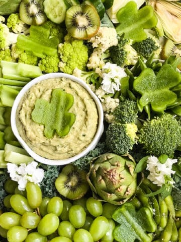 A green relish tray filled with all green vegetable and a green dip with a shamrock garnish made from bell pepper.