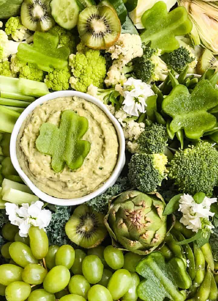 A green relish tray filled with all green vegetable and a green dip with a shamrock garnish made from bell pepper.