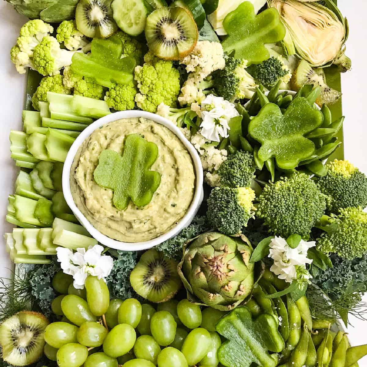 A green relish tray filled with all green vegetable and a green dip with a shamrock garnish made from bell pepper.
