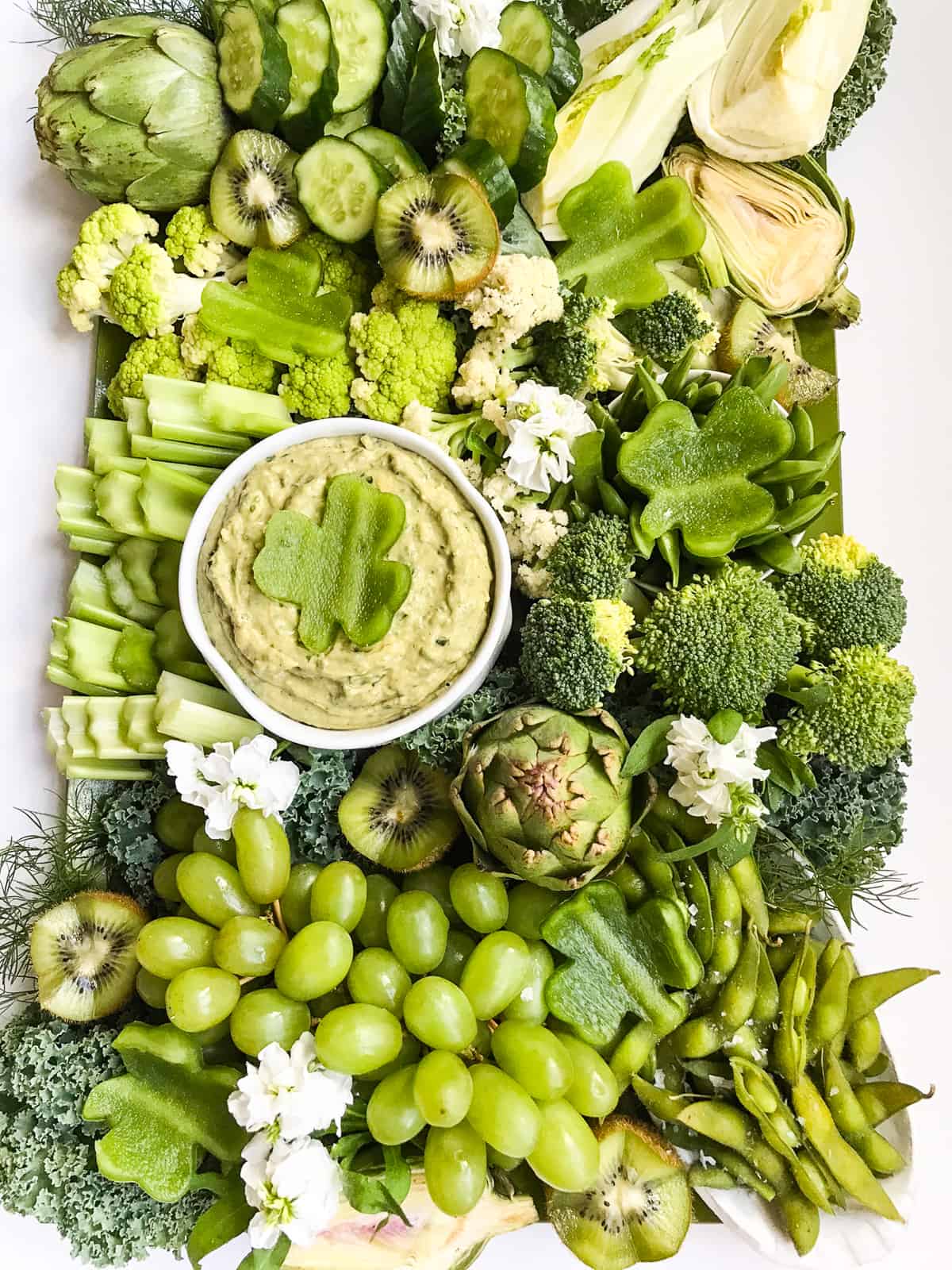 A large tray of green vegetables and a green dip with a shamrock cut out of green bell pepper.