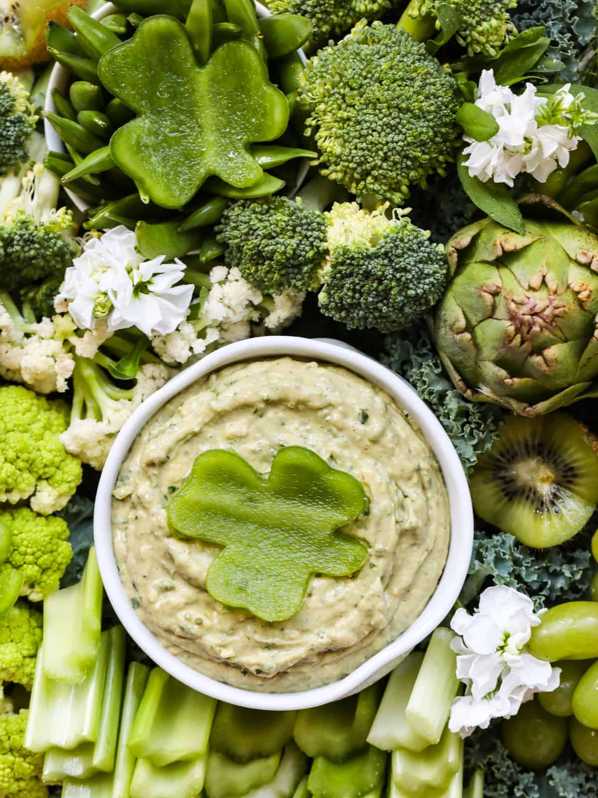 An all green St. Patrick's Day vegetable tray with a small white dish of green dip garnished with a shamrock cut from bell pepper. 