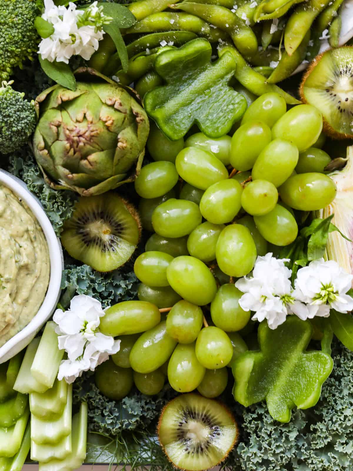 Shiny green grapes, shamrock shaped pieces of bell pepper and more green vegetables on a snack tray with a green dip.