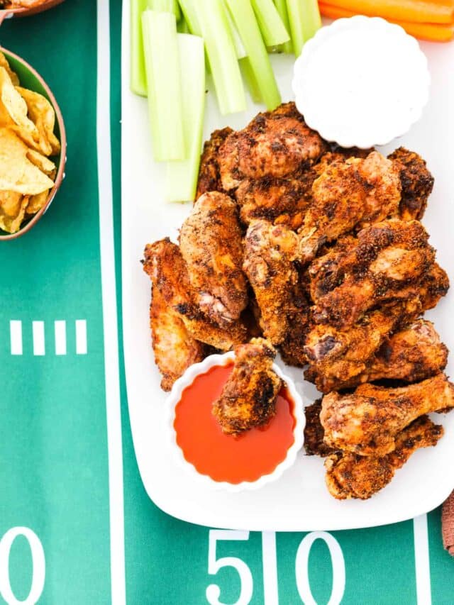 Looking over a platter of golden chicken wings with one dipped into buffalo sauce.
