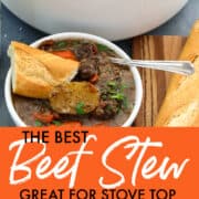 A large white cast iron pot filled with beef stew and two white bowls of stew with silver spoons and pieces of baguette bread.