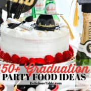 A white and red cake with a graduation cap and all kinds of party food and drinks nearby.