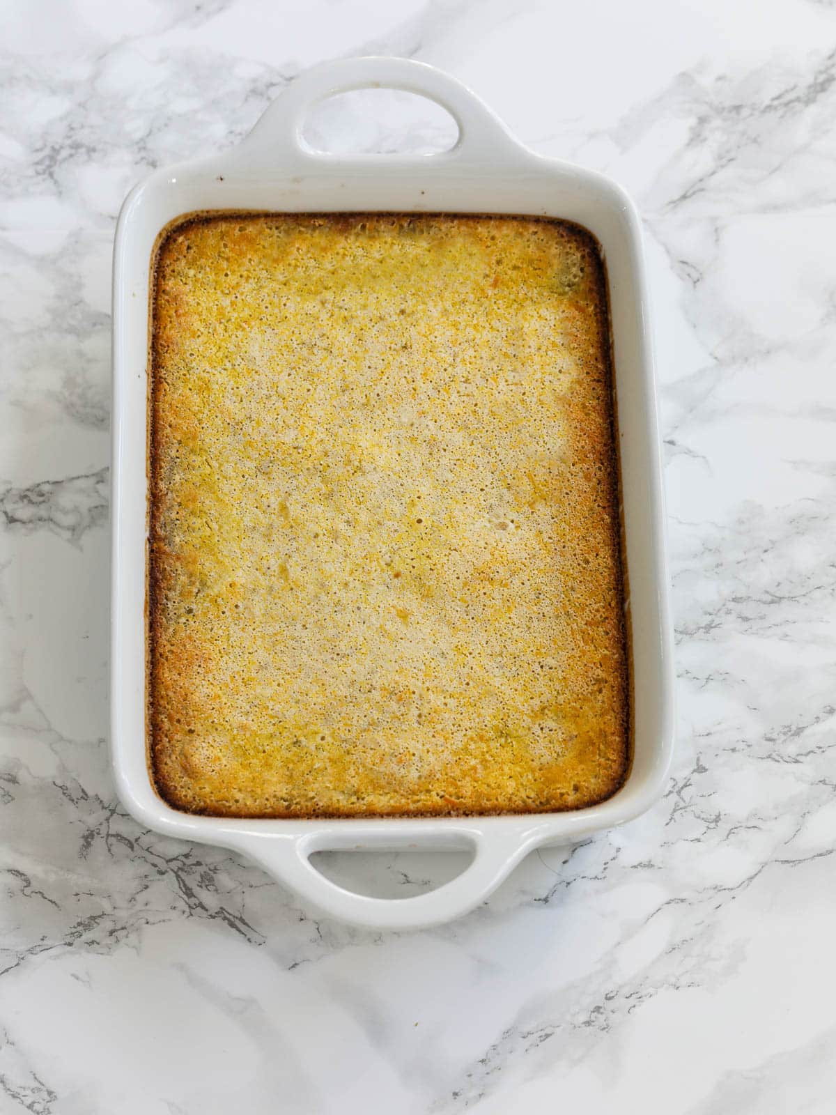 A small white baking dish filled with baked lemon bars just out of the oven.