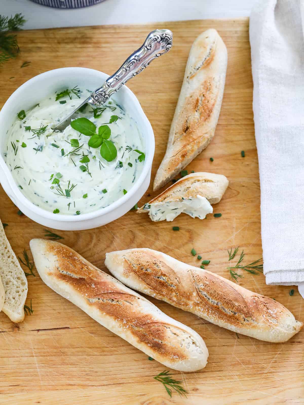 Homemade Boursin cheese spread on a piece of warm baguette bread on a cutting board. 