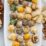 A white platter filled with cheese truffles (mini cheese balls) with crackers and pretzels at a party.