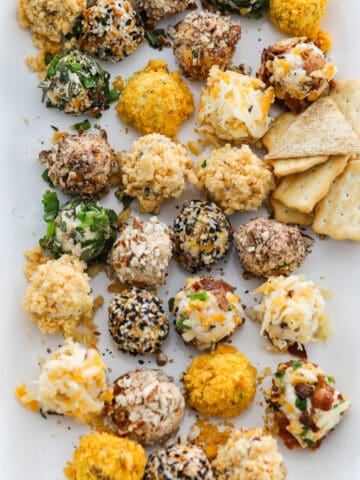 A white platter filled with cheese truffles (mini cheese balls) with crackers and pretzels at a party.