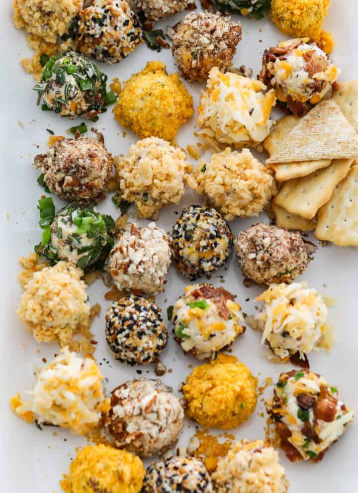 A white platter filled with cheese truffles (mini cheese balls) with crackers and pretzels at a party.