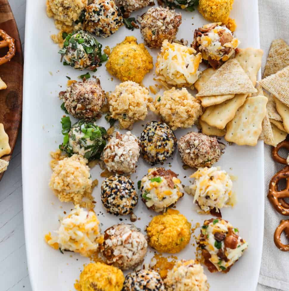 A white platter filled with cheese truffles (mini cheese balls) with crackers and pretzels at a party.