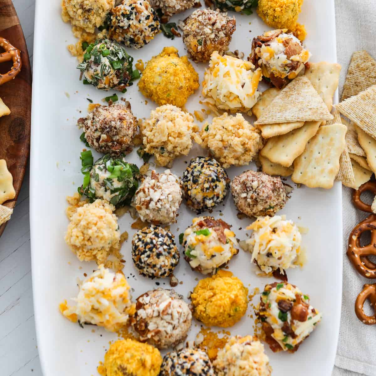 A white platter filled with cheese truffles (mini cheese balls) with crackers and pretzels at a party.