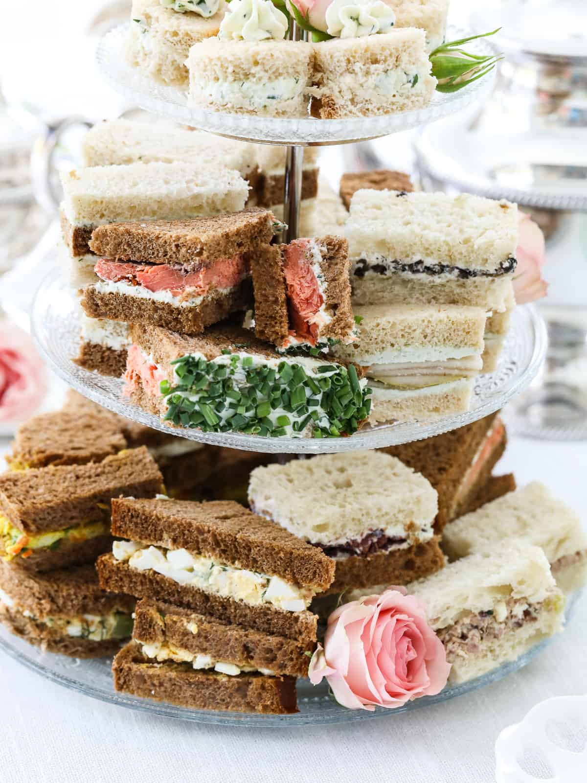 A selection of different flavors of tea sandwiches on a tiered glass tray.