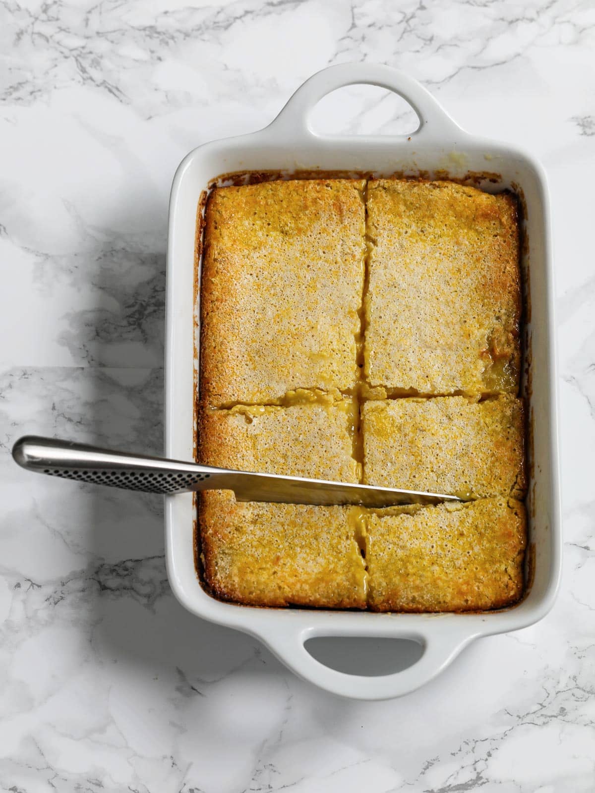 A pan of fresh baked lemon bars with a knife stuck cutting them into bars. 