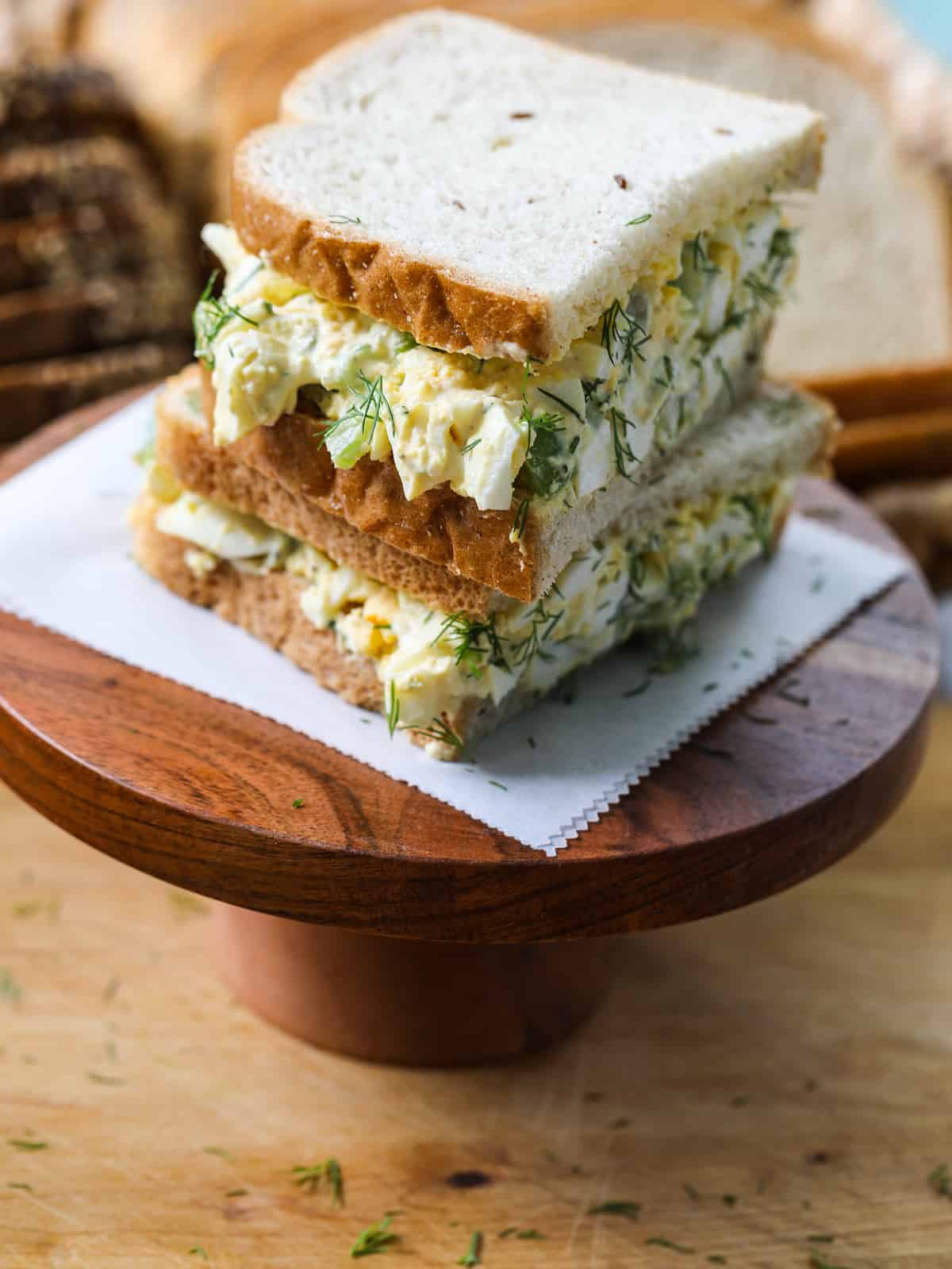Egg salad on white sandwich bread cut in half on a wood stand.