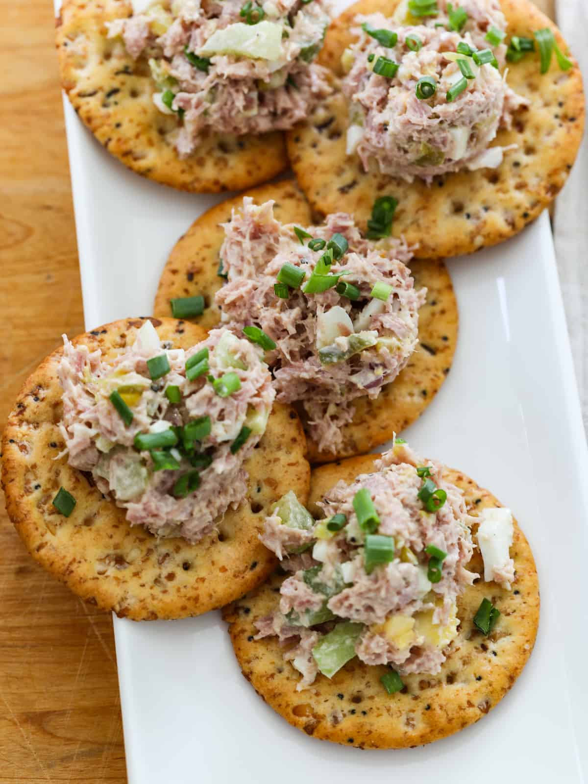 Ham salad scooped on round seeded crackers garnished with chives for an easy snack.